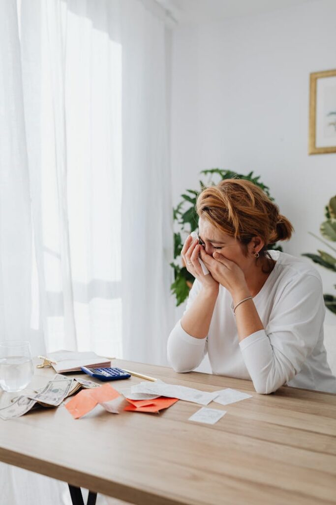Crafting Captivating Headlines: Your awesome post title goes here A woman sitting at a desk, overwhelmed by financial stress, with bills and calculator in a bright room.